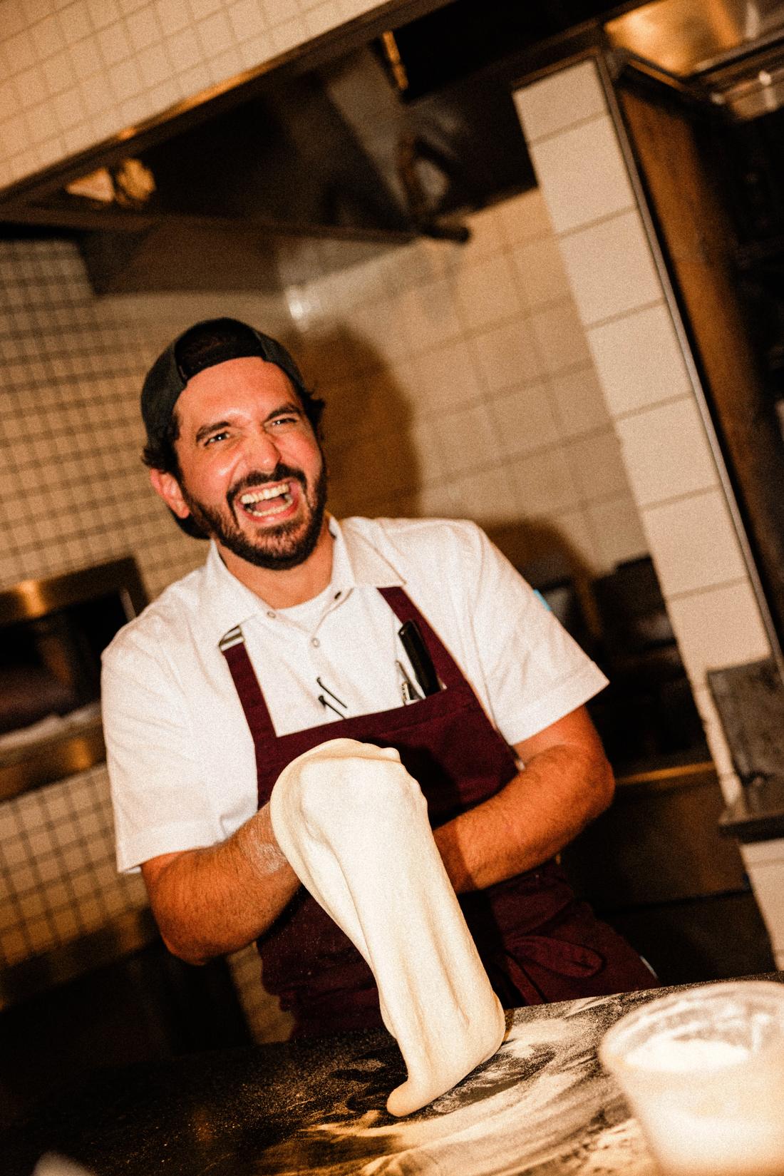 A chef laughing as he stretches pizza dough